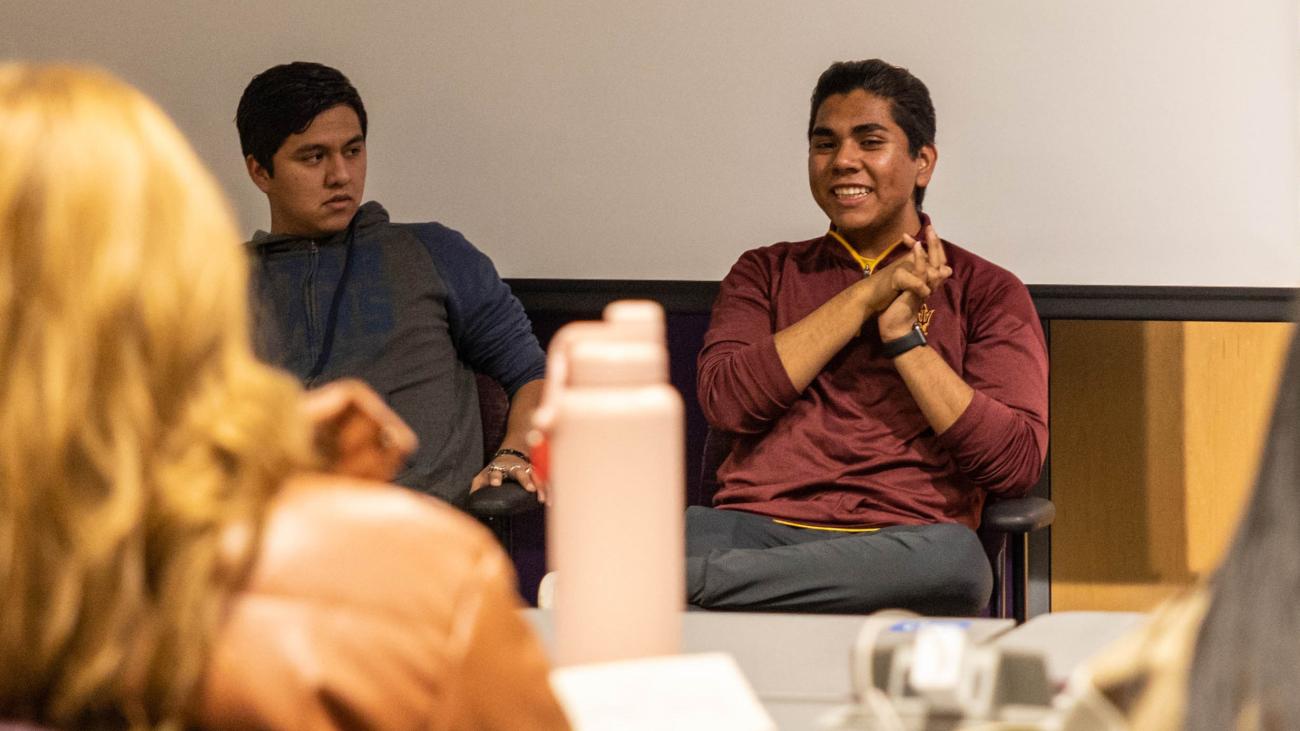 Two students sit at the front of a room and give a presentation. 